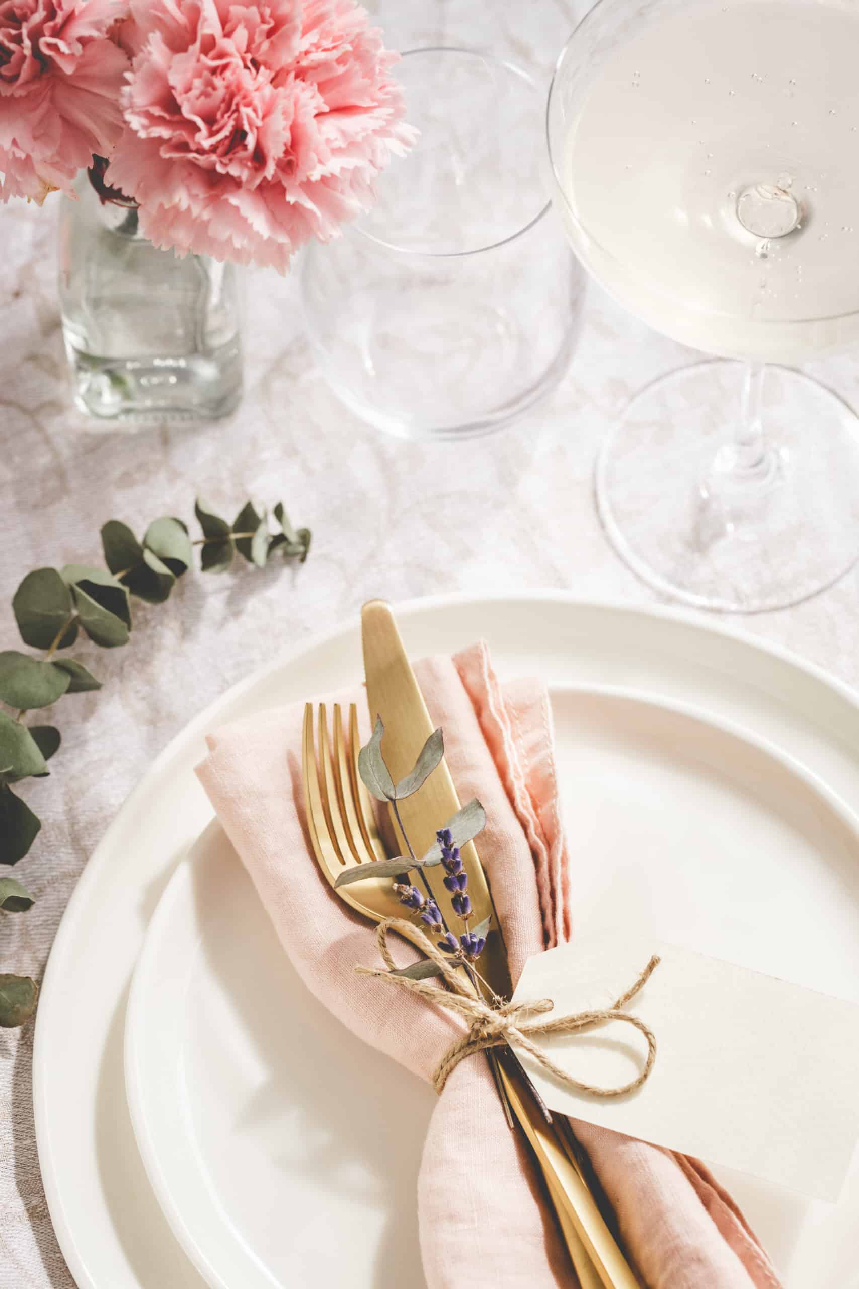 Overhead view on table setting with golden cutlery decorated with branch of eucalyptus and carnations.