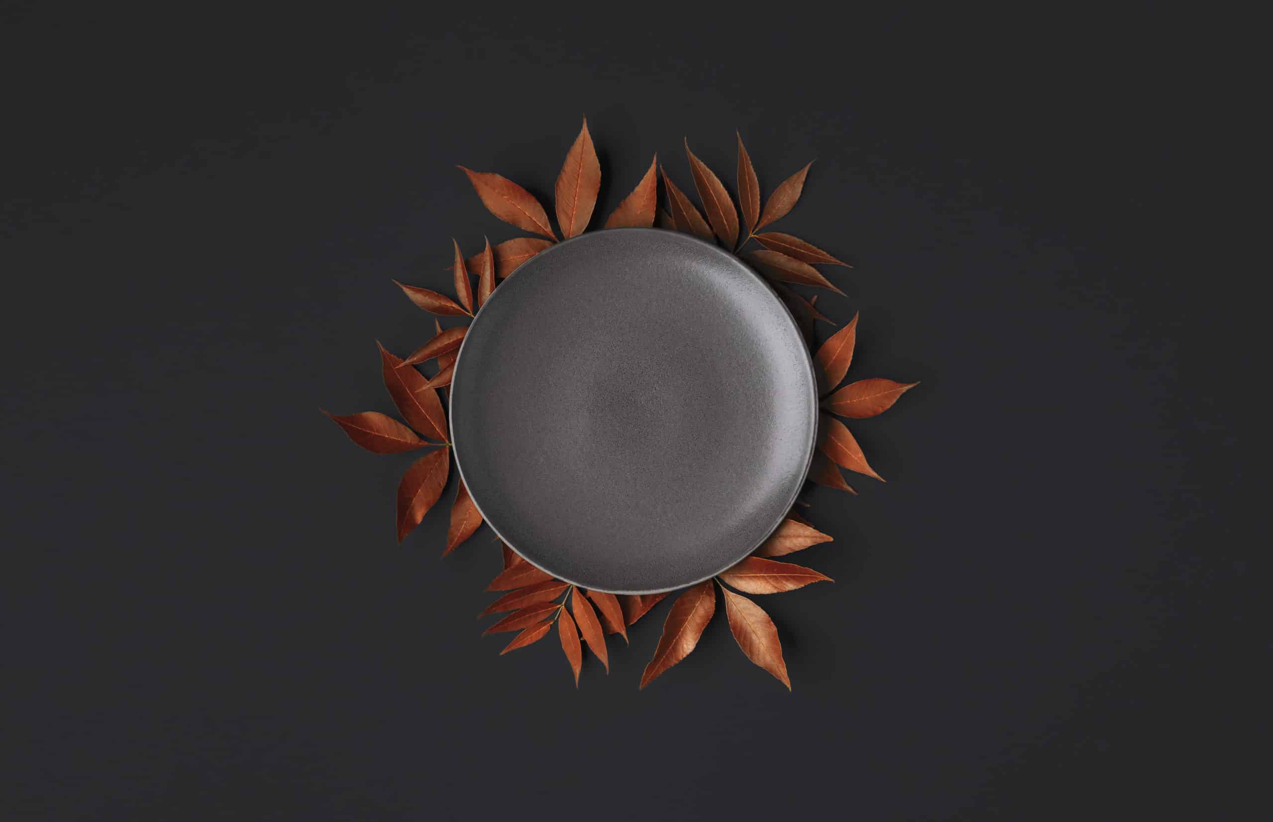 Thanksgiving table with an empty grey plate and orange leaves decoration on a black background. Autumn food background. Above view of an empty dish.