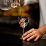 Male bartender in white shirt pours cocktail from glass with strainer