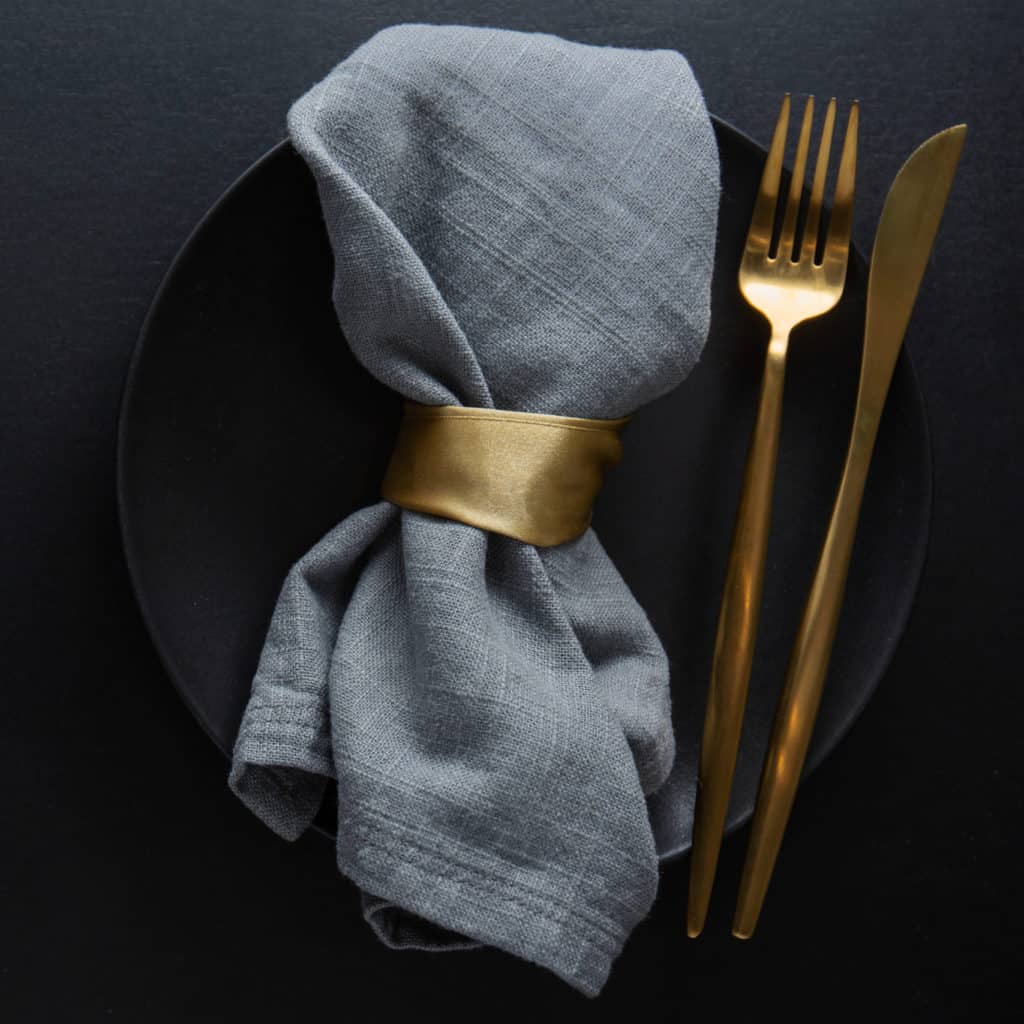Golden cutlery with textile on plate on dark background. Top View.