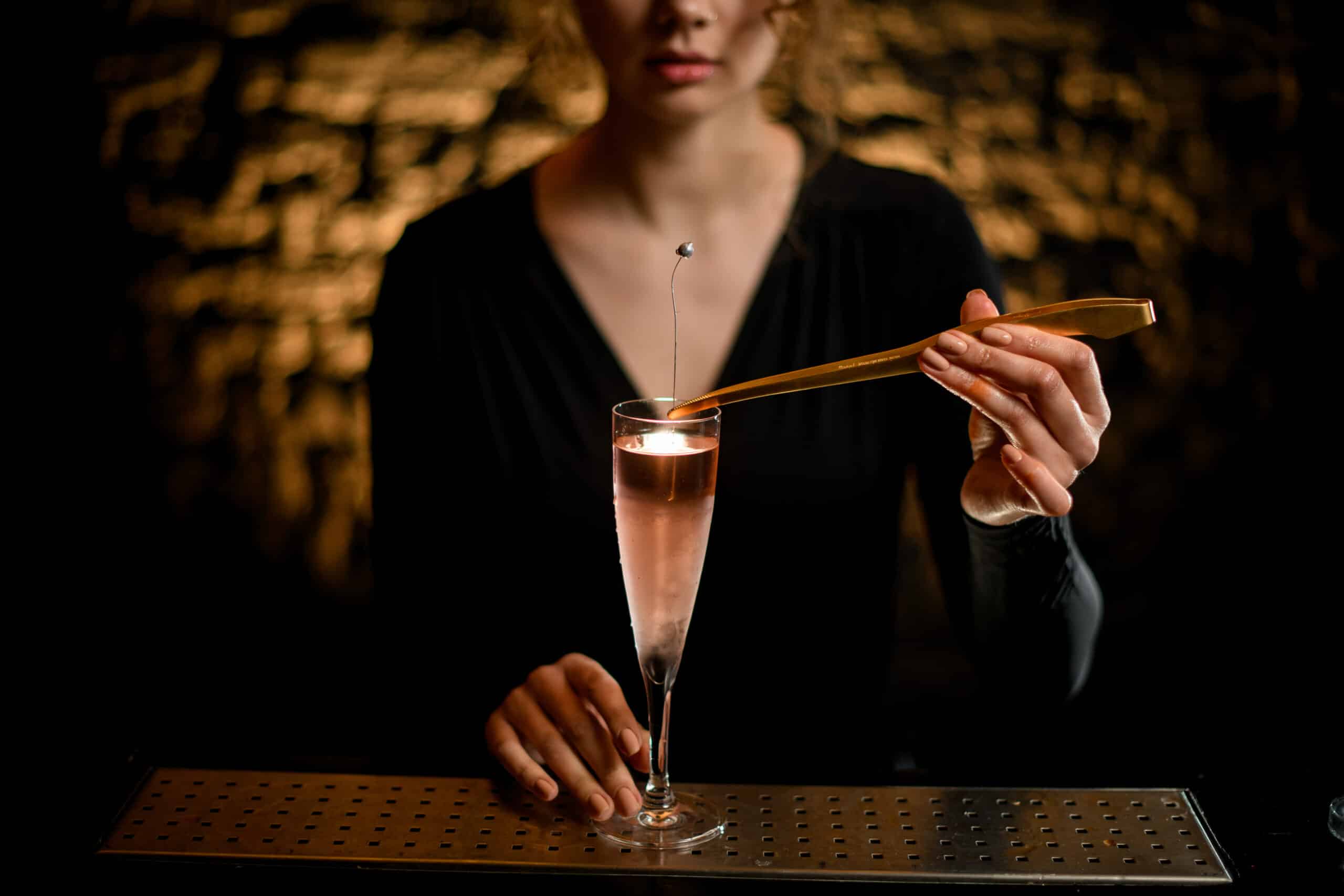 close-up girl at bar hold glass with light rose cocktail and decorates it by flower