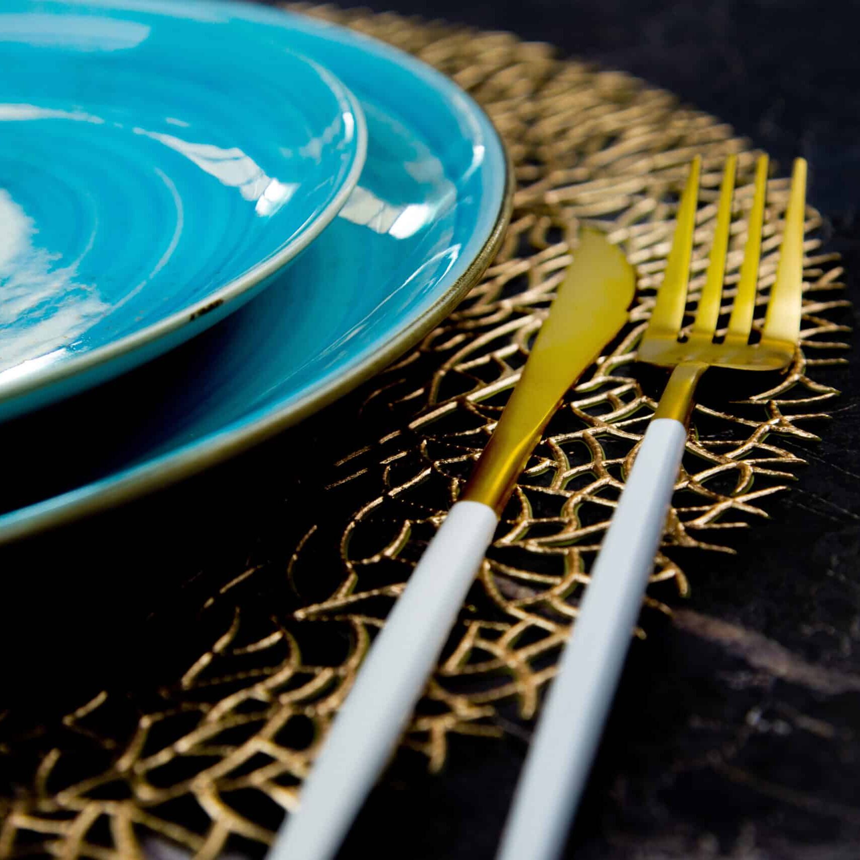 A view of half of the blue plates are standing one on one on a gold patterned napkin, gold cutlery is lying on the side: a fork and a knife on a black background with a place for text. The concept of serving, the culture of eating. High quality photo
