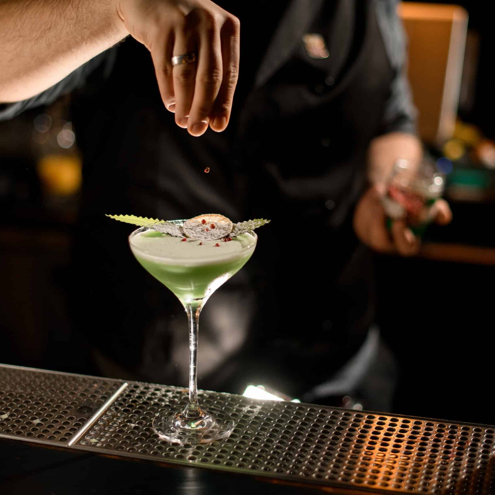 Male bartender dropping berries on a alcohol drink with eucalyptus and lemon slice
