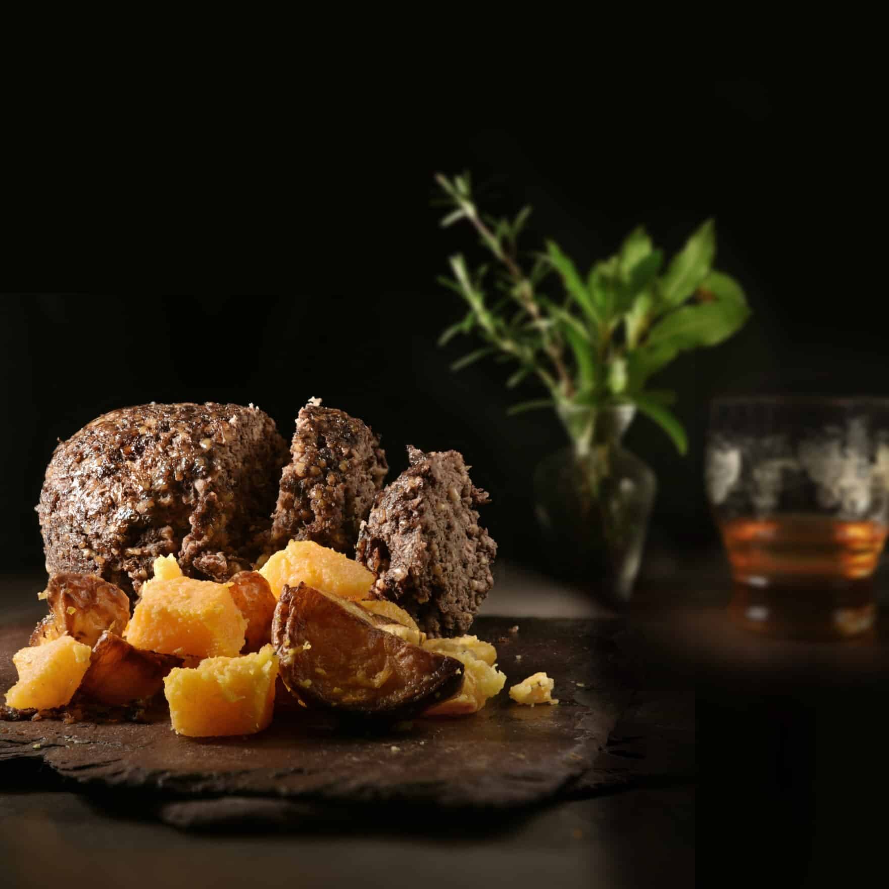 Traditional Scottish Haggis, Neeps, Tatties and Whisky shot against a dark rustic background with generous accommodation for copy space.