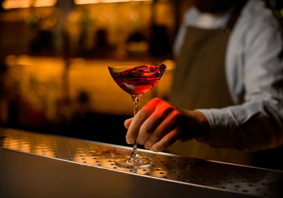 great view of wine glass with splashing drink stands on steel bar surface and male hand holds it. Blurred background.