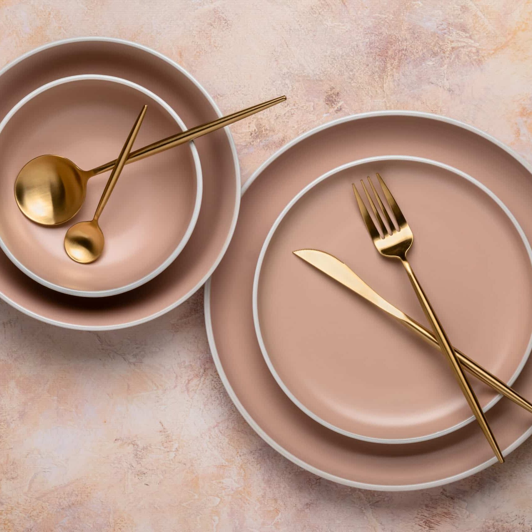 Collection of round beige plates of different sizes on the table, top view. Golden cutlery and crockery for serving and eating. Modern craft ceramic tableware, trendy tableware